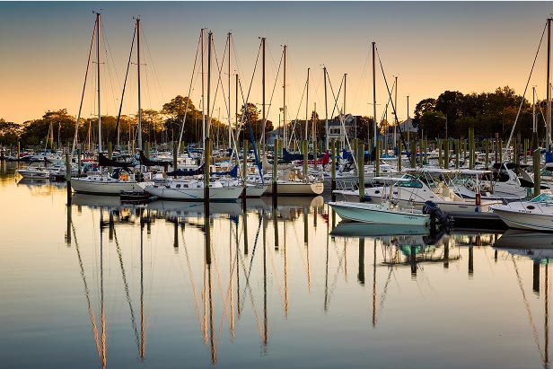 Sunset over a marina with docked sailboats and yachts reflecting in the calm waters.