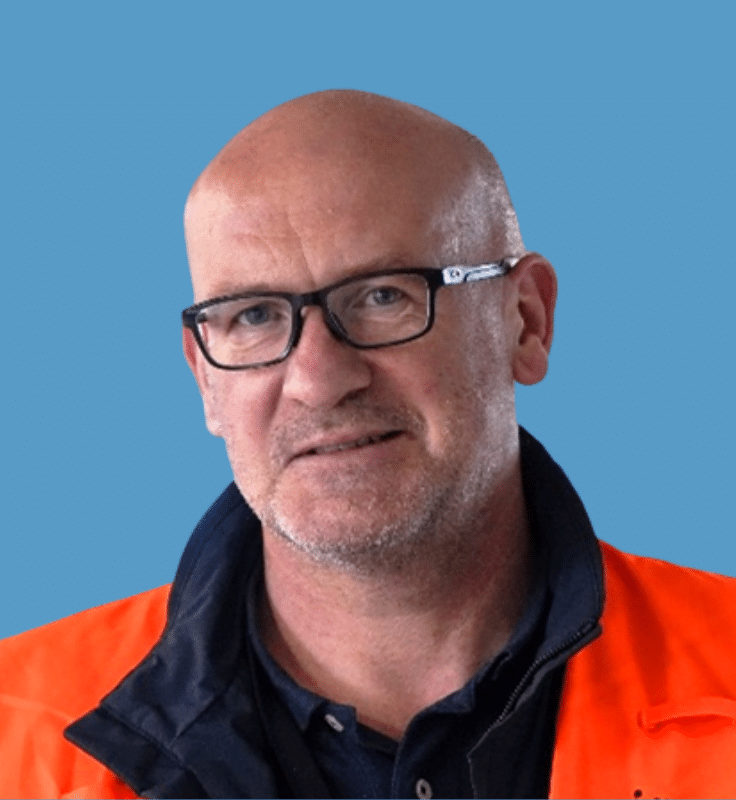 bald man with glasses, black shirt, and orange vest against blue background